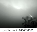 A man stands on an observation deck in the midst of heavy fog.