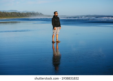 
A Man Stands On The Sand At Long Beach In Tofino, Vancouver Island, BC, Canada. A Reflection Of A Man In The Water.