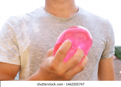 A Man Stands Outdoors And Holds A Plastic Water Bomb In His Hand - Playful Cooling In The Summer By A Balloon Full Of Water