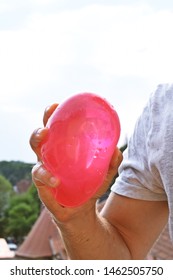 A Man Stands Outdoors And Holds A Plastic Water Bomb In His Hand - Playful Cooling In The Summer By A Balloon Full Of Water