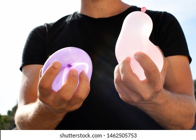 A Man Stands Outdoors And Holds A Plastic Water Bomb In His Hand - Playful Cooling In The Summer By A Balloon Full Of Water