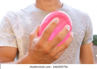 A Man Stands Outdoors And Holds A Plastic Water Bomb In His Hand - Playful Cooling In The Summer By A Balloon Full Of Water