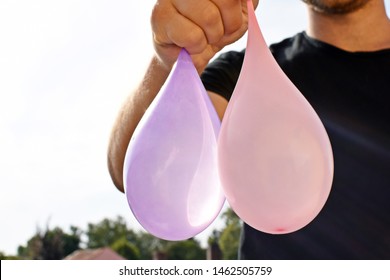 A Man Stands Outdoors And Holds A Plastic Water Bomb In His Hand - Playful Cooling In The Summer By A Balloon Full Of Water