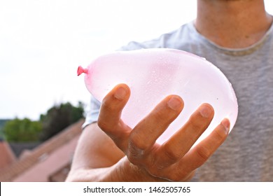 A Man Stands Outdoors And Holds A Plastic Water Bomb In His Hand - Playful Cooling In The Summer By A Balloon Full Of Water