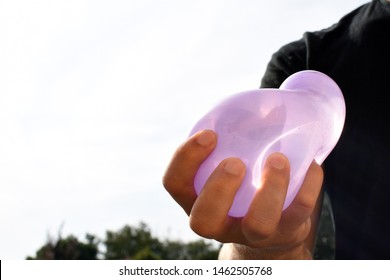 A Man Stands Outdoors And Holds A Plastic Water Bomb In His Hand - Playful Cooling In The Summer By A Balloon Full Of Water