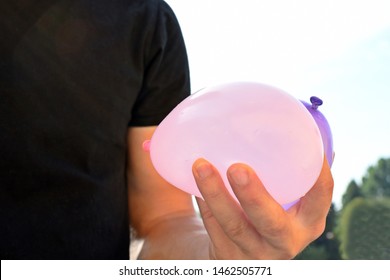 A Man Stands Outdoors And Holds A Plastic Water Bomb In His Hand - Playful Cooling In The Summer By A Balloon Full Of Water