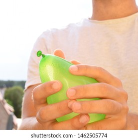 A Man Stands Outdoors And Holds A Plastic Water Bomb In His Hand - Playful Cooling In The Summer By A Balloon Full Of Water