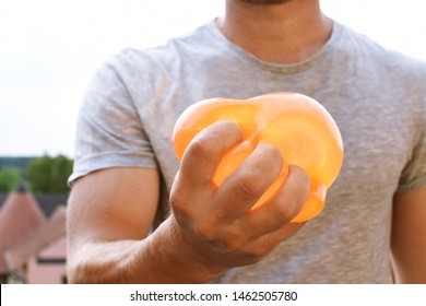 A Man Stands Outdoors And Holds A Plastic Water Bomb In His Hand - Playful Cooling In The Summer By A Balloon Full Of Water