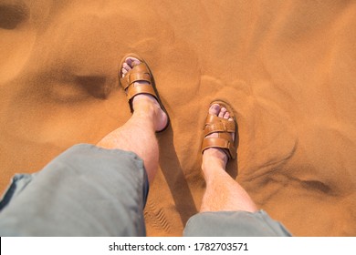 A Man Stands In Sandals On The Hot Desert Sand.