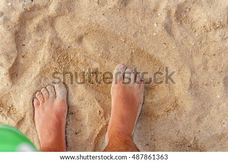 Man stands in the sea and looks at his foot in the sand and water