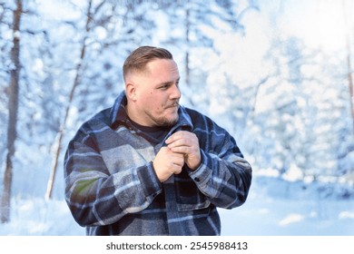 A man stands in a snowy forest, dressed warmly in a plaid coat, his expression contemplative in the chilly air. - Powered by Shutterstock