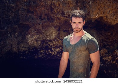 A man stands tall in front of a dark cave entrance, his figure silhouetted against the dim light filtering through. He gazes ahead, exploring the unknown depths ahead. - Powered by Shutterstock