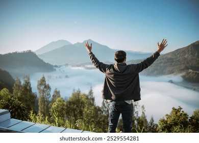 A man stands triumphantly atop a majestic mountain, his arms outstretched wide, embracing the vast landscape around him - Powered by Shutterstock