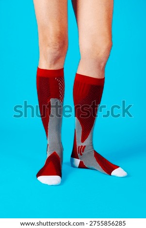 a man stands wearing red compression socks that cover the calves, supportive medical stockings designed to improve circulation and reduce leg fatigue, against a blue background