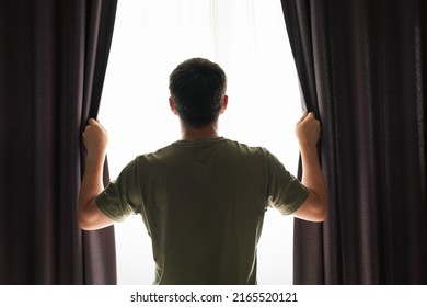 Man stands at the window and opens curtains back view. - Powered by Shutterstock