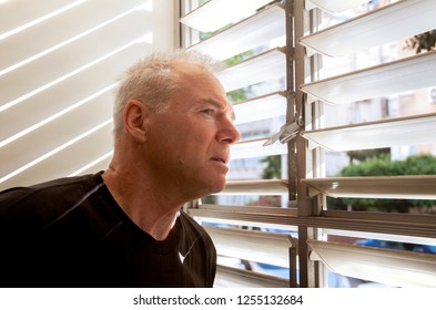 man stares out the window through the blinds