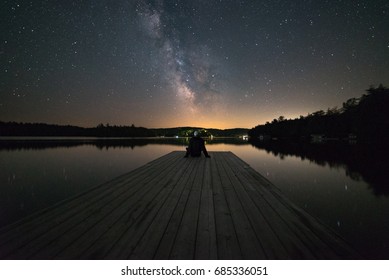Man Stargazing At The End Of A Dock In Muskoka, Ontario, Canada.