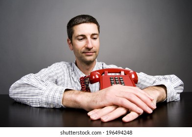 A Man Staring At A Red Phone That Is Sitting On A Table.