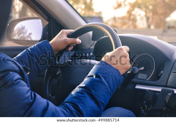 Man\
starts driving a car. Hand are on wheel. Sunny\
day