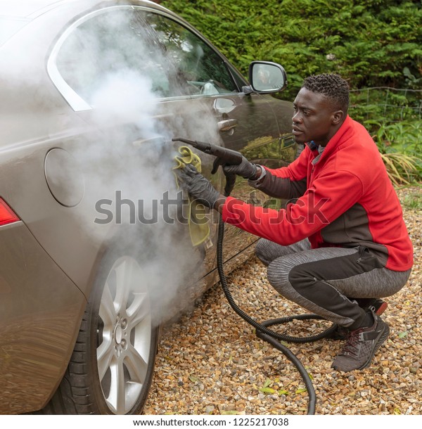 Man steam cleaning a luxury car on a home\
visiting valet service, England\
UK