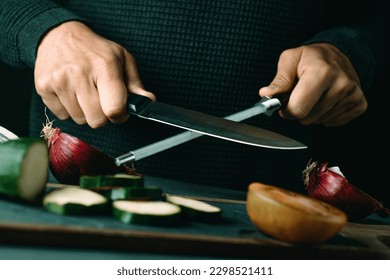 a man steels a kitchen knife with a honing steel at a table with some vegetables