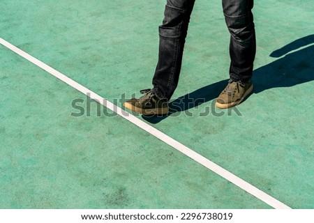 Man stepping over a white line on a green rubberized ground.Walking across the start line representing business and life start up concept. Add your own motivational quote.