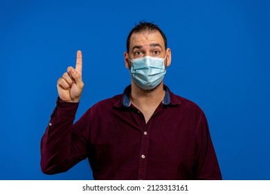 Man with sterile face mask posing isolated on blue background studio portrait. Epidemic pandemic rapidly spreading coronavirus 2019-ncov sars covid-19 flu virus concept. Point index finger up - Powered by Shutterstock