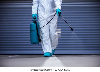 Man In Sterile Protective Suit And Mask Disinfecting Surface While Walking Towards Camera.