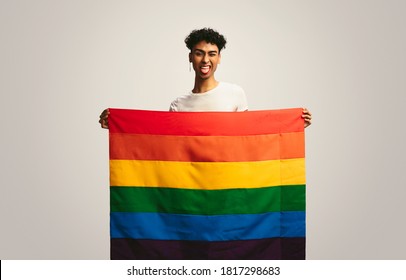 Man Sticking Out Tongue And Winking Holding Pride Flag. Gay Man With Lgbt Flag Making Funny Face On White Background.