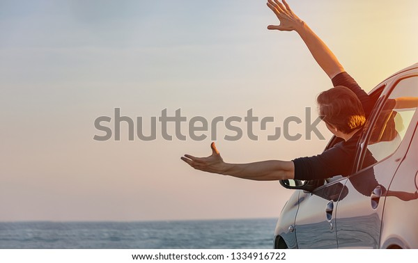 Man sticks\
out car window with raised hands, greeting, blurred sea on\
background. Road travel concept. Copy\
space.