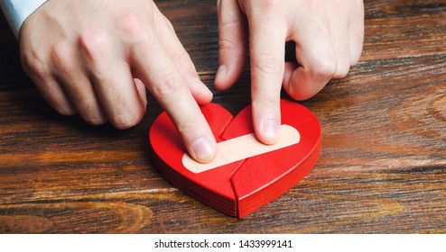 A man sticks together a red heart with a plaster. Renewal of the relationship. Family psychotherapist services. Reconciliation. Saving the family. Search for compromises. Conflict, dispute resolution