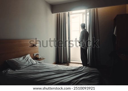 Man stood looking out the window of dingy hotel room in Porto, Portugal 