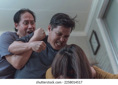 A man stops and holds back a furious guy from hitting his abused wife. Trying to pull apart a fighting couple. Example of domestic abuse. - Shutterstock ID 2258014517