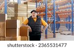 Man in storage building. Owner of warehouse business. Shelves with pallets behind worker. Man is storekeeper. Owner of warehouse company looks at camera. Guy is standing in warehouse building.