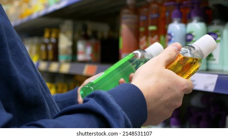 A man in a store chooses a shower gel, carefully reads the composition, then puts one bottle on the shelf and puts the other in a shopping cart for purchase. Choosing a shampoo in a supermarket - Powered by Shutterstock