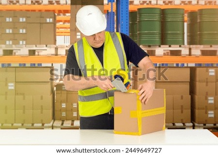 Man storekeeper. Warehouse worker packs goods. Storekeeper uses tape dispenser. Warehouse contractor in yellow vest. Storekeeper near shelves with parcels and barrels. Fulfillment company specialist