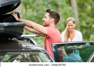 Man stows luggage in the roof box in the car before traveling on vacation
