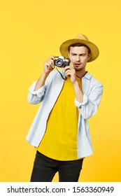 A man in a straw hat holding a camera in his hand and a cropped view of a yellow background - Shutterstock ID 1563360949