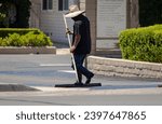A man in a straw hat spreading new asphalt slurry 