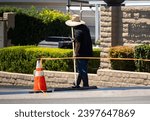 A man in a straw hat spreading new asphalt slurry 