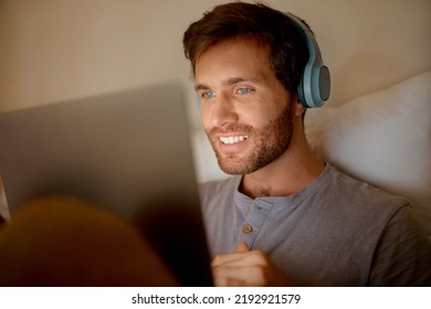 Man Streaming Movies Online On Digital Tablet, Watching Series On Technology In Bedroom And Listening To Audio On Headphones At Night In Bed At House. Person With Smile Reading Social Media Post