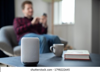 Man Streaming Music Or Podcast To Smart Speaker From Mobile Phone At Home