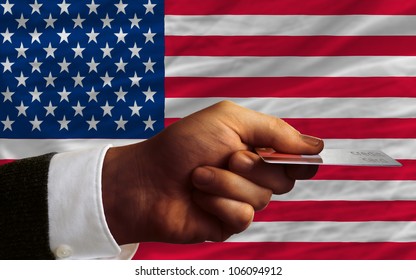 Man Stretching Out Credit Card To Buy Goods In Front Of Complete Wavy National Flag Of United States Of America