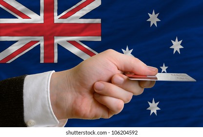 Man Stretching Out Credit Card To Buy Goods In Front Of Complete Wavy National Flag Of Australia