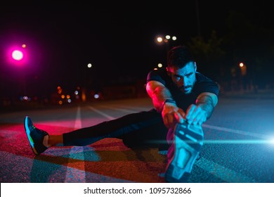 Man stretching at park while listening to music. Young man working out at nights. Healthy sport man doing stretching exercise at nights. - Powered by Shutterstock