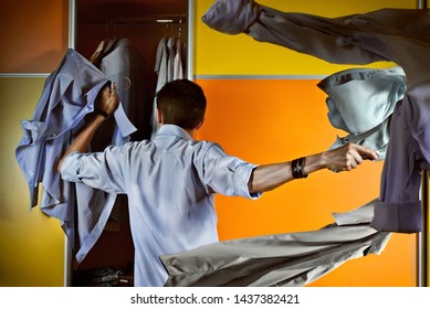 A man in a striped shirt tries clothes on the background of the closet. Yellow and orange wardrobe. The guy throws his shirts in different directions. Concept of clothing selection and fitting. - Powered by Shutterstock