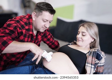A man strokes the belly of a pregnant woman and knocks with baby socks. Happy pregnant couple. A family is expecting a child. Conscious pregnancy concept - Shutterstock ID 2394565353