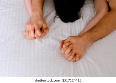 Man is stroking woman's hands lying in bed with white linen making love, hands close-up. Sex, intimate life, pleasure and love concept. Two lovers having a sex holding hands, sensual gesture.
