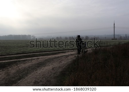 A man with a stroller in the green goggy field in the autumn