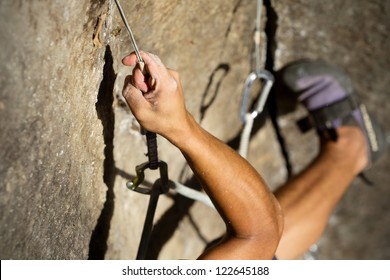 A man with strong muscles and sweating palms climbs a steep rock face, secured by a rope above. The adrenaline of the sport is palpable. - Powered by Shutterstock